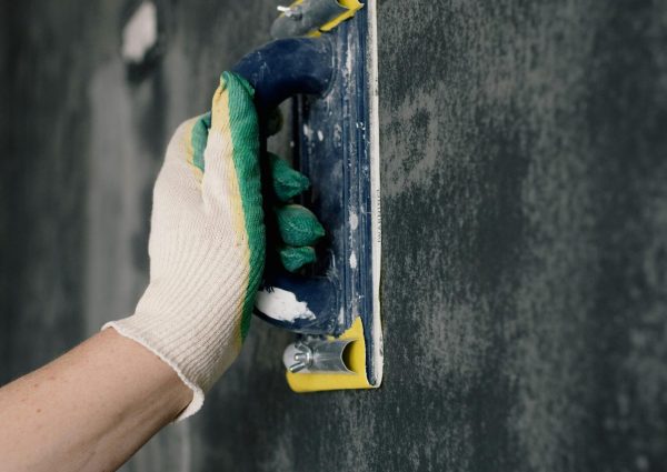 Crop anonymous male worker in gloves holding scraper and aligning walls in flat